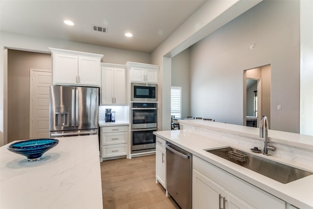 518 Syracuse St, Haslet, TX 76052 - kitchen with appliances with stainless steel finishes, a sink, white cabinetry, light stone countertops, and light wood-type flooring