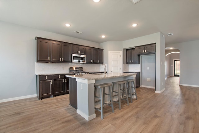 2151 Slow Stream Dr, Royse City, TX 75189 - kitchen featuring appliances with stainless steel finishes, arched walkways, a sink, backsplash, and light wood-type flooring