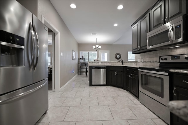 606 Brandt St, Grandview, TX 76050 - kitchen with stainless steel appliances, a chandelier, a peninsula, dark cabinetry, and tasteful backsplash