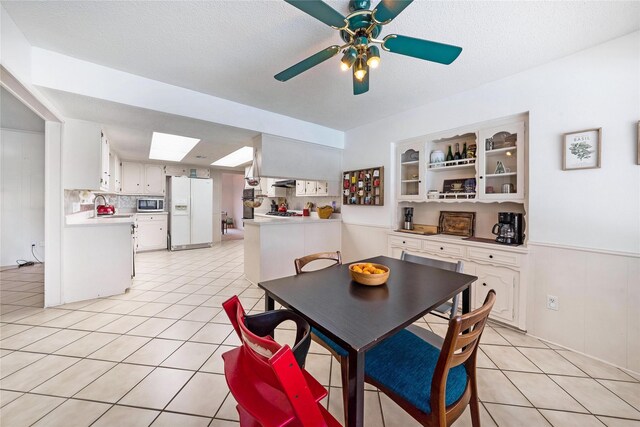 1715 Venetian Cir, Arlington, TX 76013 - dining area featuring a skylight, ceiling fan, light tile patterned floors, a textured ceiling, and wainscoting