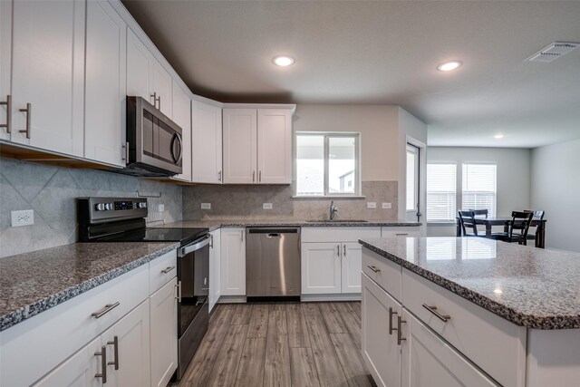 1609 Silas Dr, Forney, TX 75126 - kitchen with stainless steel appliances, a sink, light wood-type flooring, white cabinetry, and stone counters