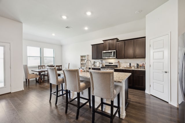 152 Whitetail Way, Caddo Mills, TX 75135 - kitchen with stainless steel appliances, dark brown cabinets, a center island with sink, a breakfast bar, and dark wood-style flooring