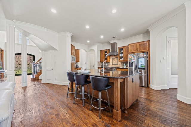 3413 De Vinci Dr, Plano, TX 75074 - kitchen featuring stainless steel appliances, wall chimney exhaust hood, arched walkways, brown cabinets, and a kitchen breakfast bar