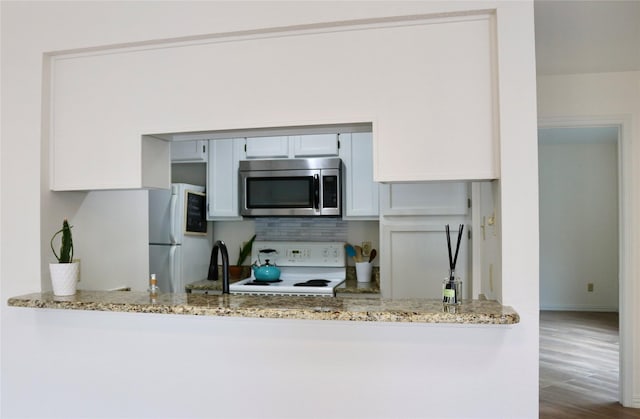 5616 Preston Oaks Rd Unit 508, Dallas, TX 75254 - kitchen with white appliances, light stone counters, backsplash, a peninsula, and wood finished floors