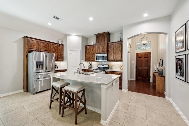 5104 Fringetree Dr, Mckinney, TX 75071 - kitchen featuring appliances with stainless steel finishes, a sink, arched walkways, light tile patterned floors, and a kitchen bar