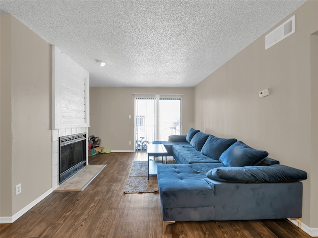 9170 Forest Ln Unit 228, Dallas, TX 75243 - living room with heating unit, a textured ceiling, dark wood-type flooring, a tiled fireplace, and baseboards