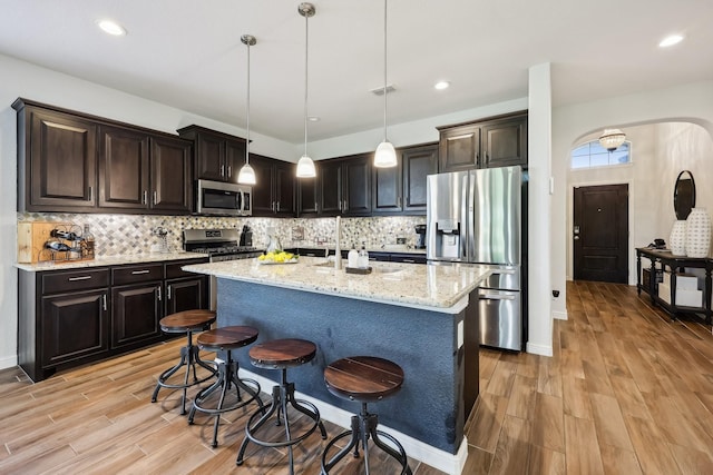 632 Dunster Ln, Saginaw, TX 76131 - kitchen featuring appliances with stainless steel finishes, arched walkways, light wood-style floors, light stone counters, and backsplash