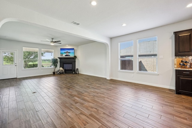 632 Dunster Ln, Saginaw, TX 76131 - unfurnished living room featuring arched walkways, ceiling fan, a glass covered fireplace, wood finished floors, and recessed lighting