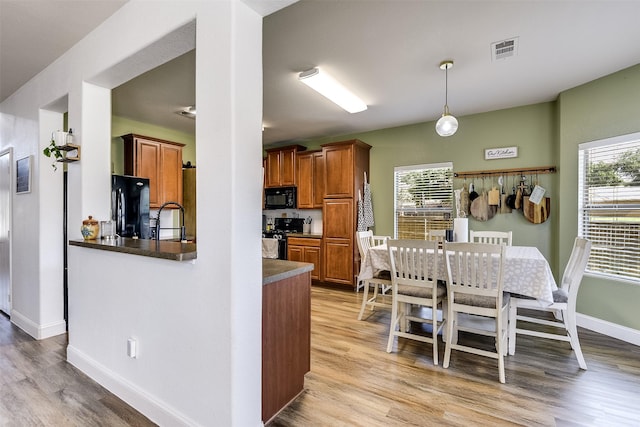 712 Saddleway Dr, Fort Worth, TX 76179 - kitchen with black appliances, light wood finished floors, brown cabinets, dark countertops, and decorative light fixtures