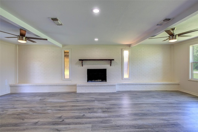 552 Oak Leaf Trl, East Tawakoni, TX 75472 - unfurnished living room featuring ceiling fan, brick wall, a fireplace, beam ceiling, and wood finished floors