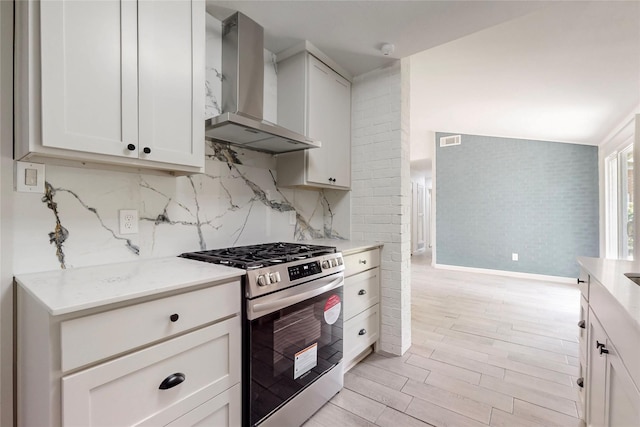 409 Fleming Dr, Hurst, TX 76053 - kitchen with wall chimney range hood, stainless steel gas range oven, light wood-style flooring, baseboards, and decorative backsplash