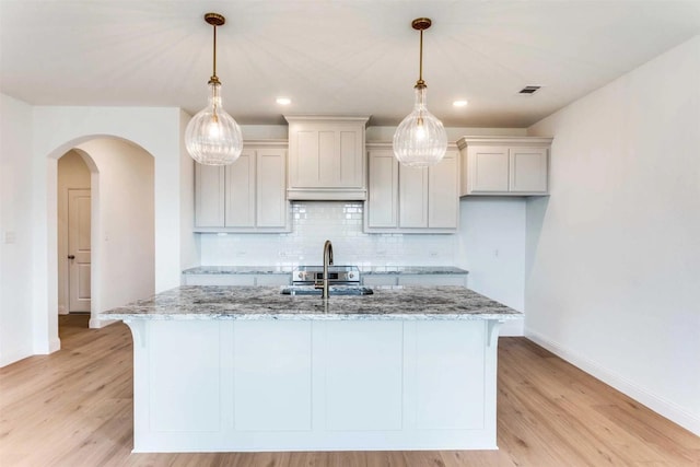533 Hillcrest Cir, Justin, TX 76247 - kitchen with baseboards, a sink, light stone counters, tasteful backsplash, and a center island with sink