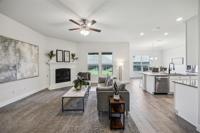 6217 Cheshire St, Celina, TX 76227 - living area with a glass covered fireplace, wood finished floors, a chandelier, baseboards, and a ceiling fan