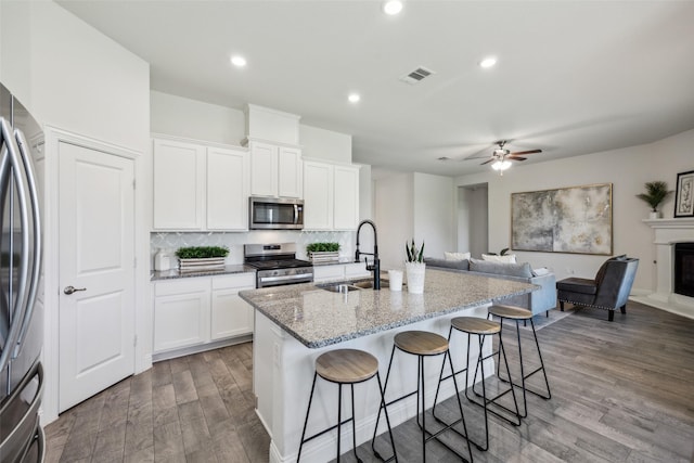 6217 Cheshire St, Celina, TX 76227 - kitchen with appliances with stainless steel finishes, a sink, light stone counters, wood finished floors, and a kitchen bar
