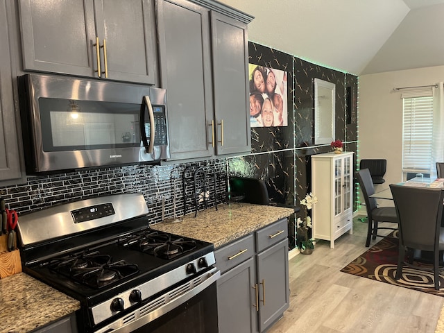 1311 Rosler St, Mansfield, TX 76063 - kitchen featuring appliances with stainless steel finishes, gray cabinets, lofted ceiling, light wood-style flooring, and light stone countertops