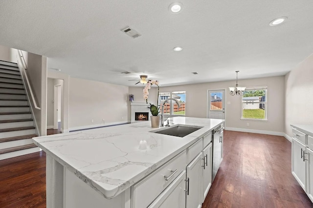 1409 Nicholas Ln, Little Elm, TX 75068 - kitchen with a sink, a warm lit fireplace, ceiling fan, dark wood-type flooring, and white cabinets
