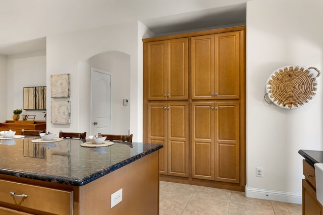 307 Sagebrush Dr, Oak Point, TX 75068 - kitchen featuring dark stone counters, brown cabinets, light tile patterned flooring, arched walkways, and baseboards