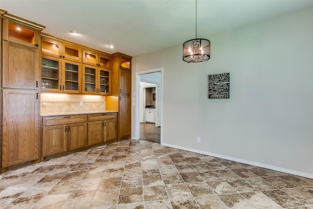 206 Crooked Creek Dr, Richardson, TX 75080 - kitchen featuring brown cabinetry, a chandelier, stone finish flooring, decorative backsplash, and glass insert cabinets