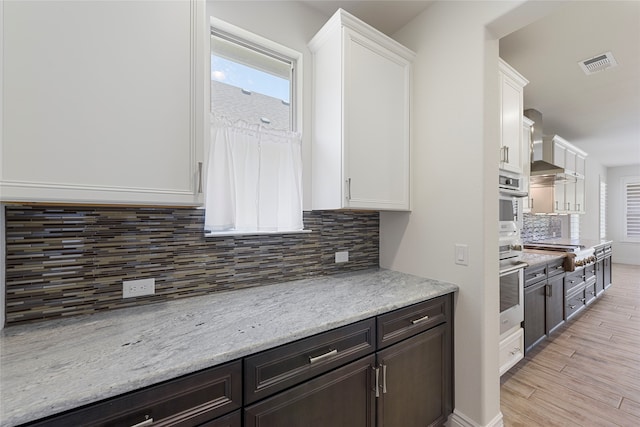 9921 Flint Way, Denton, TX 76207 - kitchen with white cabinets, wall chimney exhaust hood, decorative backsplash, light wood-style flooring, and stainless steel gas stovetop