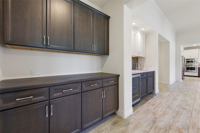 9921 Flint Way, Denton, TX 76207 - kitchen with beverage cooler, dark brown cabinetry, stainless steel double oven, ornamental molding, and light wood-style floors