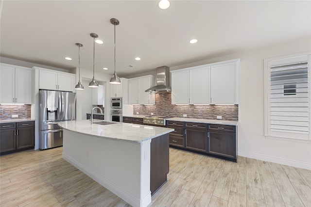 9921 Flint Way, Denton, TX 76207 - kitchen with appliances with stainless steel finishes, wall chimney exhaust hood, a sink, light wood-style flooring, and tasteful backsplash