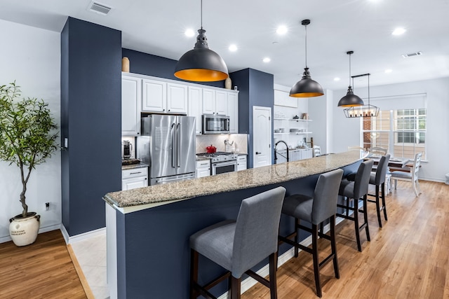 15763 Spectrum Dr Unit 93, Addison, TX 75001 - kitchen with appliances with stainless steel finishes, a kitchen bar, an island with sink, white cabinetry, and light stone counters