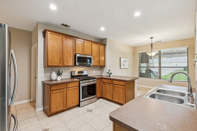 1702 Travis Ct, Allen, TX 75002 - kitchen featuring appliances with stainless steel finishes, a sink, decorative backsplash, brown cabinetry, and a peninsula