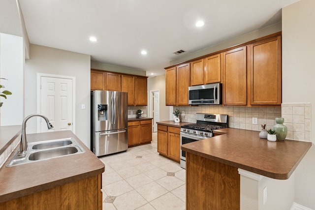 1702 Travis Ct, Allen, TX 75002 - kitchen featuring appliances with stainless steel finishes, a sink, brown cabinetry, a peninsula, and tasteful backsplash