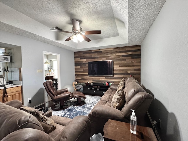 629 Yosemite Trl, Mesquite, TX 75149 - living room featuring wooden walls, a raised ceiling, a textured ceiling, ceiling fan, and carpet