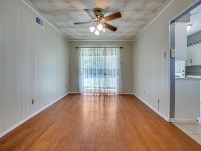 2504 W Rochelle Rd, Irving, TX 75062 - empty room with a ceiling fan, light wood-style floors, crown molding, baseboards, and wooden walls