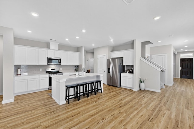 403 Pendant Dr, Royse City, TX 75189 - kitchen featuring stainless steel appliances, light wood-style floors, a breakfast bar area, tasteful backsplash, and white cabinetry