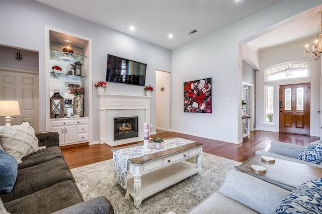 1200 Stonehedge Pl, Flower Mound, TX 75028 - living room featuring wood finished floors, arched walkways, a fireplace with raised hearth, a chandelier, and built in features