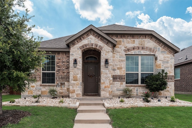 2705 Hancock Ln, Celina, TX 75009 - french country style house featuring a front yard, a shingled roof, and stone siding