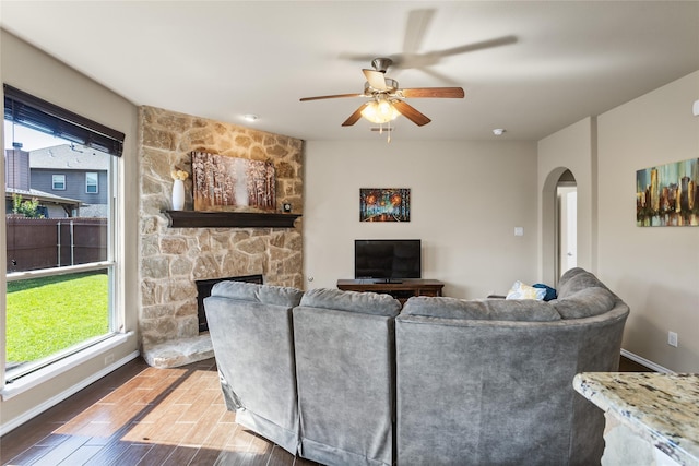 3028 Maple Creek Dr, Fort Worth, TX 76177 - living area featuring arched walkways, a stone fireplace, a ceiling fan, wood finished floors, and baseboards
