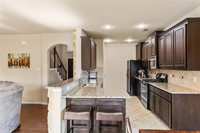 3028 Maple Creek Dr, Fort Worth, TX 76177 - kitchen featuring stainless steel appliances, a sink, a breakfast bar area, dark brown cabinets, and arched walkways