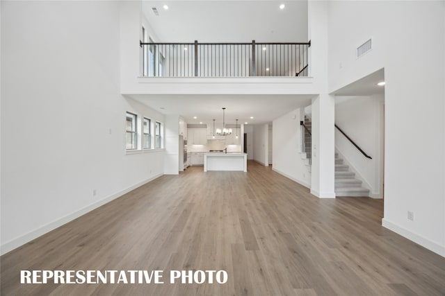 4180 Kestrel St, Prosper, TX 75078 - unfurnished living room with a high ceiling, stairs, light wood-style floors, a chandelier, and baseboards