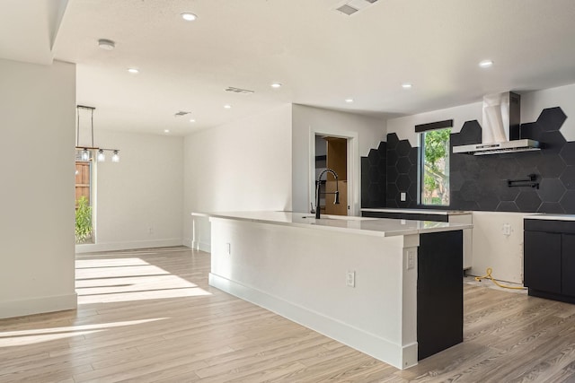 16212 Spring Creek Rd, Dallas, TX 75248 - kitchen featuring wall chimney range hood, light wood finished floors, a center island with sink, tasteful backsplash, and recessed lighting