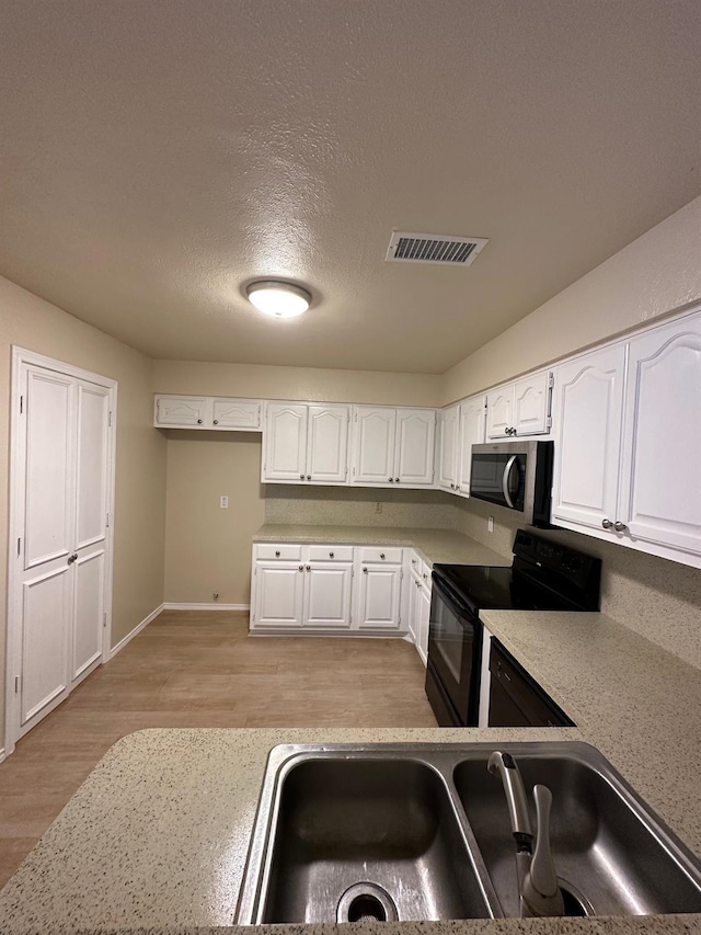 3620 Hilltop Ln, Plano, TX 75023 - kitchen featuring stainless steel microwave, black range with electric cooktop, light wood finished floors, a sink, and white cabinetry