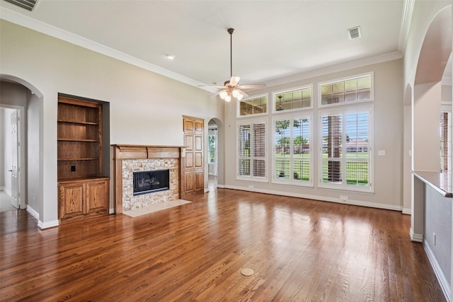 8304 Old Hickory Ln, Mckinney, TX 75072 - unfurnished living room featuring arched walkways, a stone fireplace, crown molding, wood finished floors, and a ceiling fan