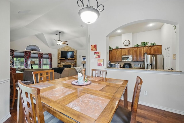14708 Myrtle Beach Ln, Frisco, TX 75035 - dining space featuring a ceiling fan, dark wood-type flooring, arched walkways, a fireplace, and vaulted ceiling