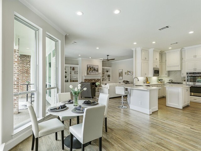 4033 Oakhaven Dr, Plano, TX 75093 - dining area with ornamental molding, light wood finished floors, a brick fireplace, recessed lighting, and ceiling fan