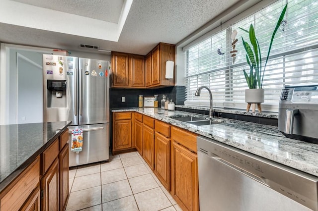 238 Browning Ln, Grand Prairie, TX 75052 - kitchen with appliances with stainless steel finishes, a sink, brown cabinets, a textured ceiling, and tasteful backsplash