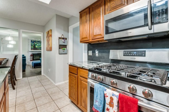 238 Browning Ln, Grand Prairie, TX 75052 - kitchen featuring stainless steel appliances, decorative backsplash, baseboards, light tile patterned flooring, and brown cabinetry