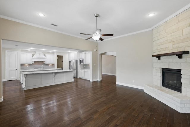 2866 Milsons Point Dr, Trophy Club, TX 76262 - unfurnished living room featuring a ceiling fan, ornamental molding, a stone fireplace, dark wood-style floors, and arched walkways