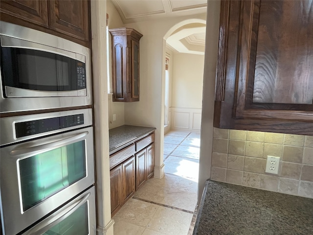 6916 Cannon Falls Dr, Plano, TX 75024 - kitchen with stainless steel appliances, dark brown cabinetry, arched walkways, decorative backsplash, and wainscoting