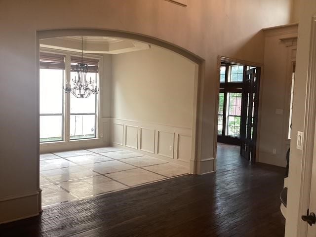 6916 Cannon Falls Dr, Plano, TX 75024 - unfurnished dining area featuring a chandelier, arched walkways, dark wood-style floors, wainscoting, and a decorative wall