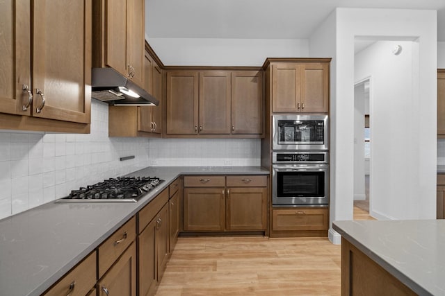 2213 Windy Hill Ln, Waxahachie, TX 75167 - kitchen featuring stainless steel appliances, under cabinet range hood, light wood finished floors, decorative backsplash, and brown cabinets