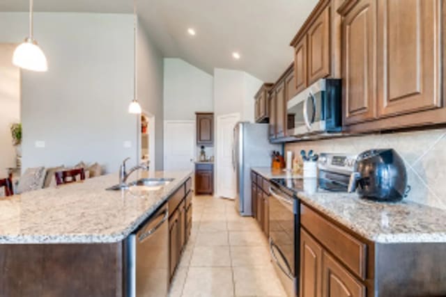 11520 Starlight Ranch Trl, Fort Worth, TX 76052 - kitchen featuring appliances with stainless steel finishes, vaulted ceiling, a center island with sink, light stone countertops, and decorative light fixtures