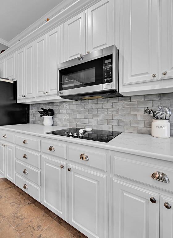 804 Heritage Pkwy, Axtell, TX 76624 - kitchen featuring stainless steel microwave, black electric stovetop, light countertops, white cabinets, and tasteful backsplash