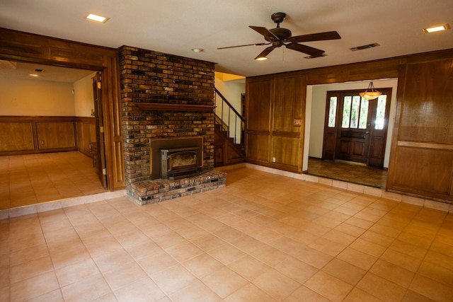 6837 Roberts Ln, Fort Worth, TX 76140 - unfurnished living room featuring wooden walls, ceiling fan, light tile patterned flooring, stairs, and a wood stove